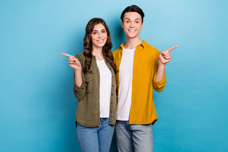 Photo of two positive smile lovely cute couple direct fingers empty space recommend new family proposition prices isolated on blue color backgroundの写真素材