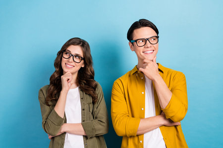 Photo of dreamy funny married couple wear shirts spectacles looking empty space arm chin isolated...