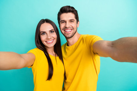 Photo of positive sweet married couple wear yellow t-shirts recording video vlog smiling isolated teal color backgroundの写真素材