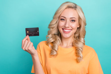 Portrait of adorable lovely person with wavy hairdo wear stylish t-shirt fingers hold credit card isolated on turquoise color backgroundの写真素材