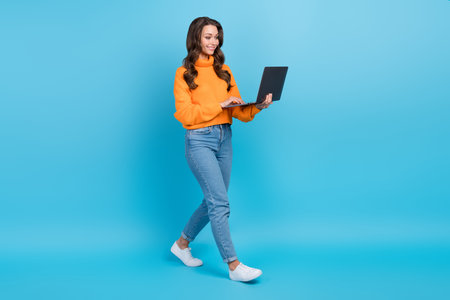 Full length photo of sweet shiny lady dressed orange pullover communicating modern device isolated blue color backgroundの写真素材