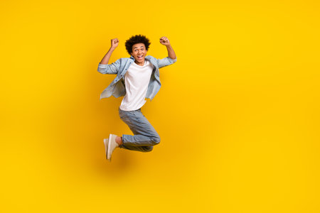Full body portrait of delighted crazy person jumping raise fists empty space isolated on yellow color backgroundの写真素材