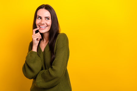 Photo of cheerful nice girl finger touch chin beaming smile look empty space isolated on yellow color backgroundの写真素材