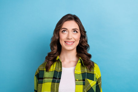 Portrait of cute pretty pleasant girl with wavy hairstyle wear plaid jacket smiling look empty space isolated on blue color backgroundの写真素材