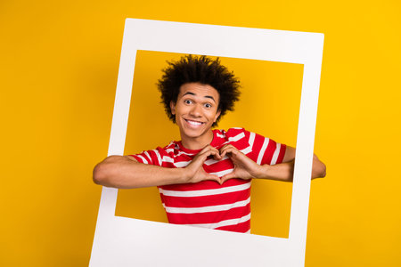 Photo of pretty cute guy wear striped t-shirt showing arms heart photographing isolated yellow color backgroundの写真素材