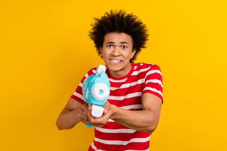 Photo of funky person biting lips hands hold water gun pistol isolated on yellow color background
