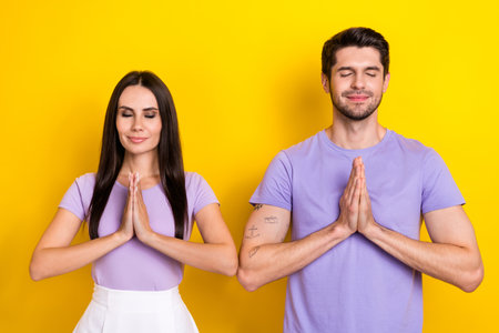 Portrait of two calm satisfied people closed eyes hands meditate retreat isolated on yellow color backgroundの写真素材