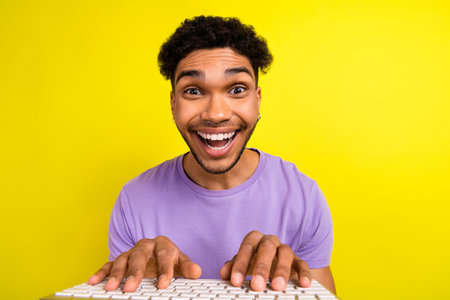 Portrait of astonished cheerful person beaming smile fingers typing keyboard isolated on yellow color backgroundの写真素材