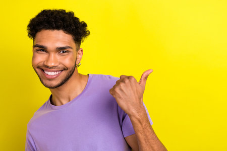 Portrait of nice friendly positive man beaming smile direct finger empty space proposition isolated on yellow color backgroundの写真素材