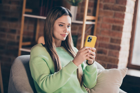 Photo of pretty positive person sitting comfy armchair use smart phone chatting typing blog post loft interior flat indoorsの写真素材