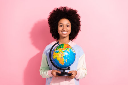Portrait of charming positive schoolchild toothy smile hands hold planet earth globe isolated on pink color backgroundの写真素材