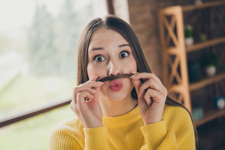 Photo of overjoyed young person hands hold hair make mustache pretend man pouted plump lips free time flat insideの写真素材