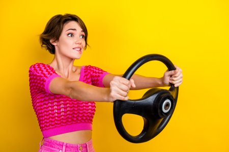 Photo of hipster girl bob brown hair bite lips panic first time driving alone hold steering wheel problem auto isolated on yellow color backgroundの写真素材