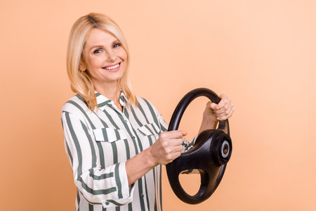 Profile photo of positive nice aged lady beaming smile arms hold wheel isolated on beige color...
