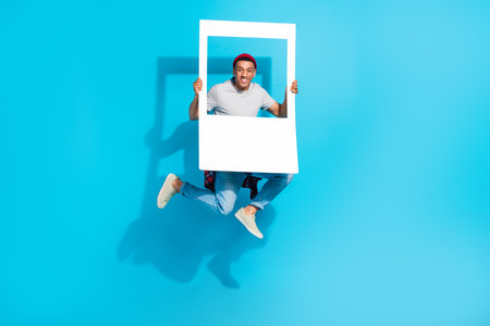 Full size portrait of carefree active person jumping arms hold paper album card isolated on blue color backgroundの写真素材