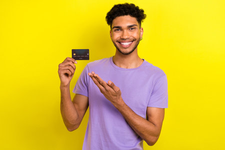 Photo of young guy hold his new premium bonus debit card directing his hand offer banking commerce isolated on yellow color backgroundの写真素材
