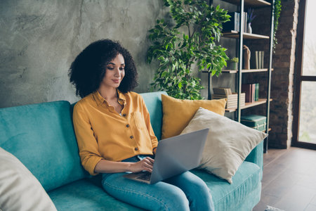 Photo of cheerful positive lady specialist dressed shirt smiling texting emails modern gadget sitting sofa indoors workstation workshopの写真素材