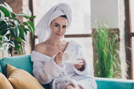 Photo of lovely lady relax after bath shower with hydration beauty product drink espresso in living roomの写真素材