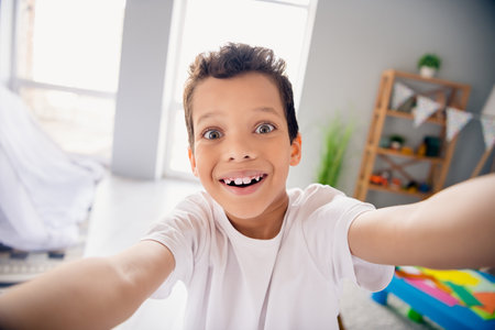 Photo of sweet pretty little boy dressed white t-shirt smiling tacking selfie indoors house home roomの写真素材