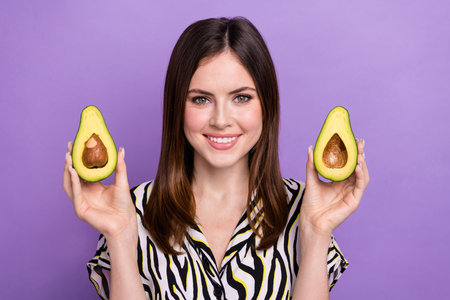 Portrait of cheerful nice girl beaming smile arms hold two halves avocado isolated on purple color backgroundの写真素材