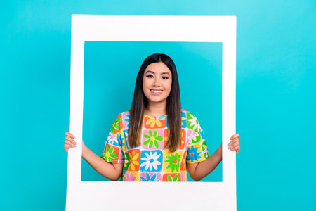 Cadre of young lady wear stylish tropical colorful t-shirt hold paper borders memories photozone isolated on aquamarine color backgroundの写真素材