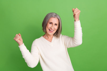 Photo of overjoyed glad pensioner woman react novelty adv raise fists win lottery free tickets trip isolated green backgroundの写真素材