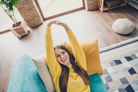 Above view portrait of pretty cheerful lady laying comfy sofa toothy smile stretching arms free time weekend modern house insideの写真素材