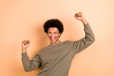 Portrait of young overjoyed man wear stylish brown jumper raise fists up shout celebrate victory shopping day isolated on beige color backgroundの写真素材