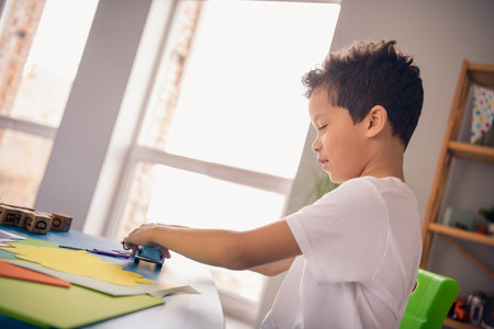 Photo of positive sweet little boy dressed white t-shirt sitting table playing car toys game indoors house home roomの写真素材