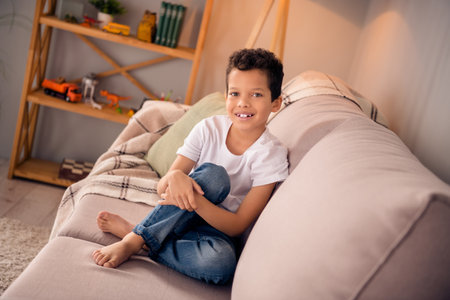 Photo of positive cheerful cute boy sit comfy divan relax after end school year in modern playroom apartmentの写真素材