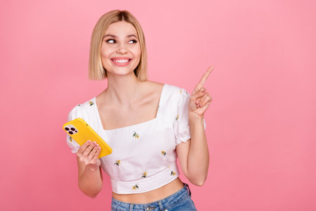 Portrait of young lady bob hair wear stylish blouse point finger look empty space smartphone web product isolated on pink color backgroundの写真素材