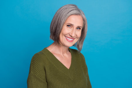 Photo of stunning aged grandmother smiling demonstrating white bleaching teeth wear khaki sweater isolated blue color backgroundの写真素材