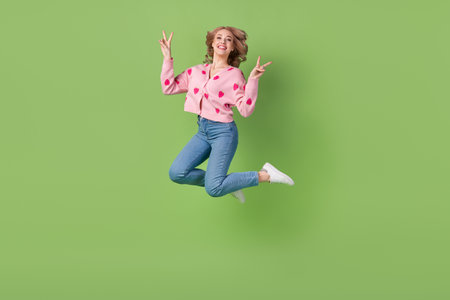 Full length cadre of woman jump have fun showing double v-sign enjoy life active lifestyle trendy outfit isolated on green color backgroundの写真素材