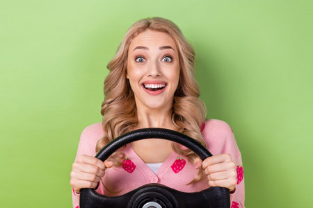 Portrait of funky astonished positive lady beaming smile arms hold wheel steering isolated on green color backgroundの写真素材