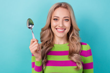 Photo of adorable pretty cute woman with curly hairstyle dressed striped sweatshirt holding spoon isolated on teal color backgroundの写真素材