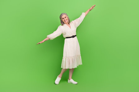 Full length photo of sweet carefree woman dressed beige outfit arms sides having fun isolated green color backgroundの写真素材