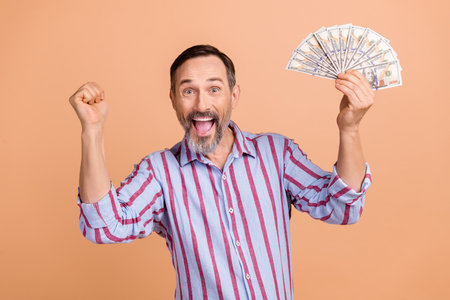 Portrait of funny overjoyed person with white gray beard hold money raising fist up win gambling isolated on pastel color backgroundの写真素材