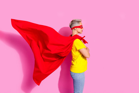 Profile photo of cool superhero girl folded arms look empty space flying red cape isolated on pink color backgroundの写真素材