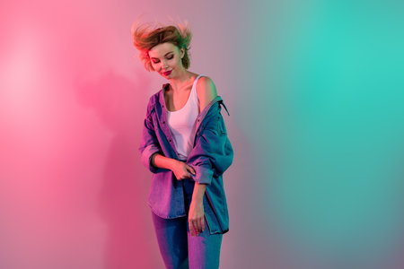 Photo of pretty shiny girl dressed jeans shirt smiling wind blowing isolated turquoise pink light...