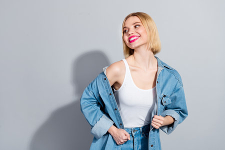 Photo of dreamy cute girl dressed jeans shirt smiling looking empty space isolated grey color backgroundの写真素材