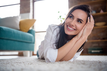 Portrait of nice thoughtful mind lady lying carpet enjoy her new house with big windows sun shine bright comfortの写真素材