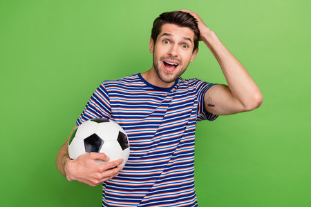 Photo of young sporty guy holding ball soccer fan  isolated on green color backgroundの写真素材