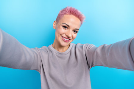 Portrait of optimistic cool lovely girl with short haircut wear gray clothes making selfie smiling isolated on blue color backgroundの写真素材