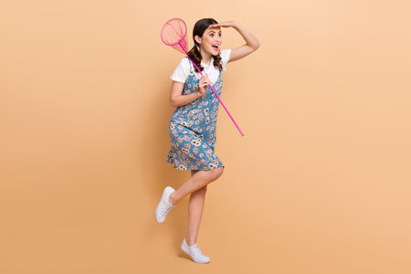 Full body photo of young overjoyed girl hand forehead try find hunt insects more research explore environment isolated on beige backgroundの写真素材