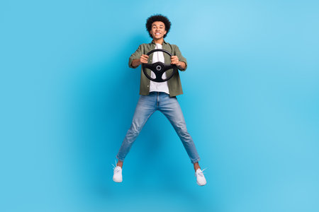 Full body photo of jumping overjoyed man hold steering wheel insurance advert hold steering wheel driver isolated on blue color backgroundの写真素材