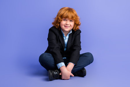 Full length photo of friendly satisfied schoolkid sit floor have good mood wear elegant uniform isolated on violet color backgroundの写真素材