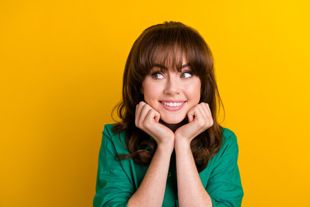 Photo of adorable dreamy lady wear green shirt arms cheeks looking empty space isolated yellow color...