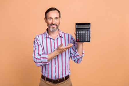 Portrait of positive satisfied elegant person arm hold demonstrate calculator numbers isolated on beige color backgroundの写真素材