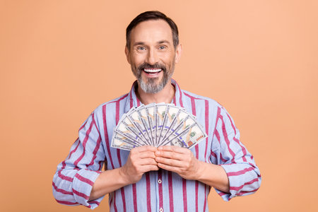 Portrait of positive elegant aged person beaming smile arms hold dollar banknotes bills isolated on beige color backgroundの写真素材