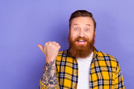 Photo of excited bearded guy hipster overjoyed direct thumb finger empty space isolated purple color backgroundの写真素材
